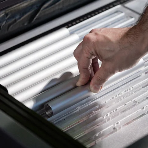 Baltensweiler: Eine Hand kontrolliert oder bearbeitet eine Anordnung länglicher transparenter beziehungsweise metallischer Bauteile.