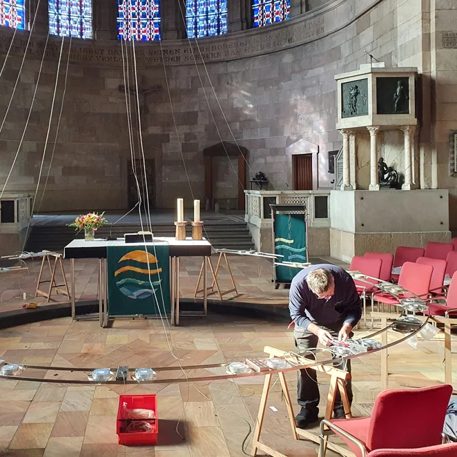 Licht im Raum: Großer aufgehängter Ring während einer Überarbeitung in einem Kirchenraum mit Arbeitsmaterialien.