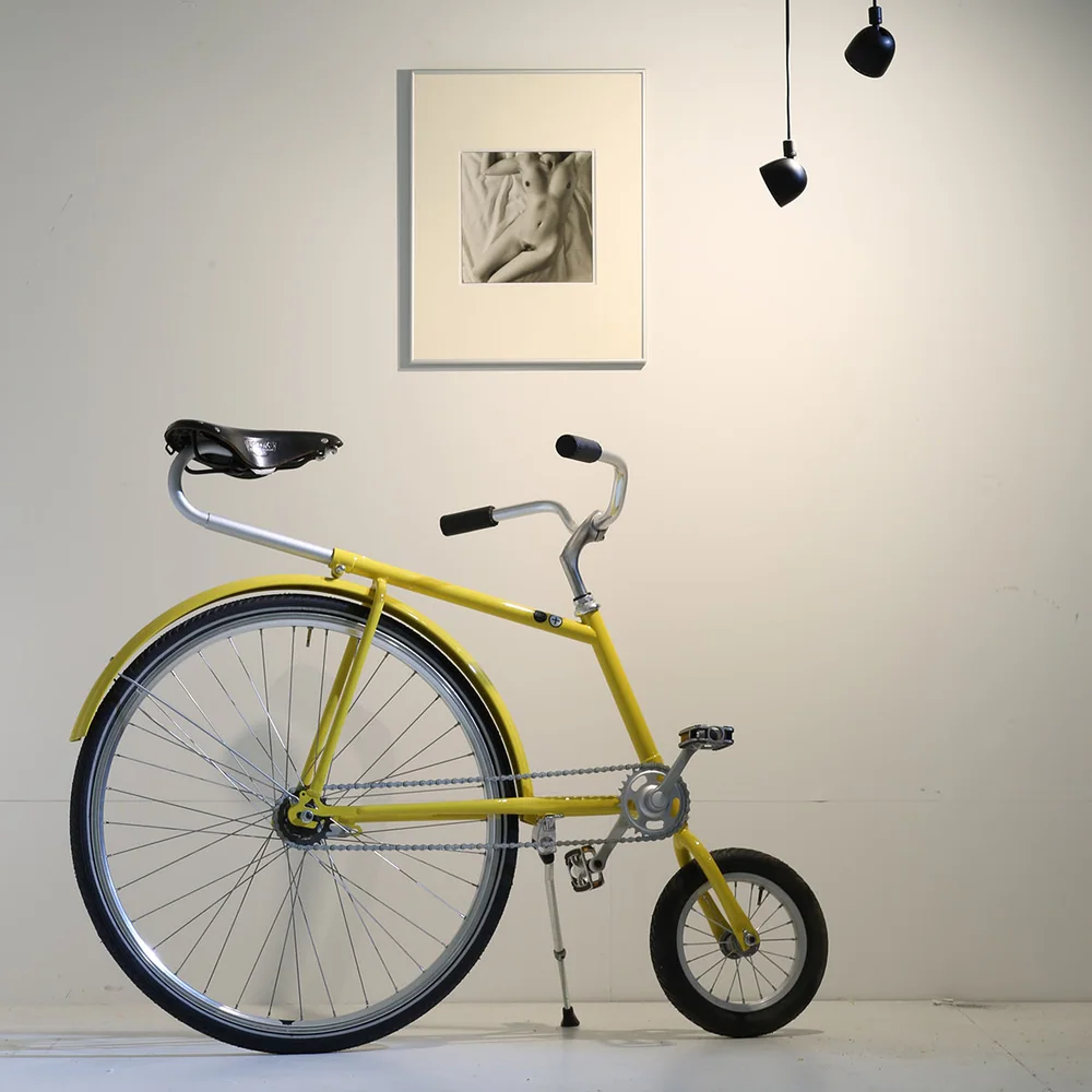 Martinelli Luce: Mehrere kleine dunkle Leuchtenkörper an langen Kabeln vor einer hellen Wand mit gelbem Fahrrad.