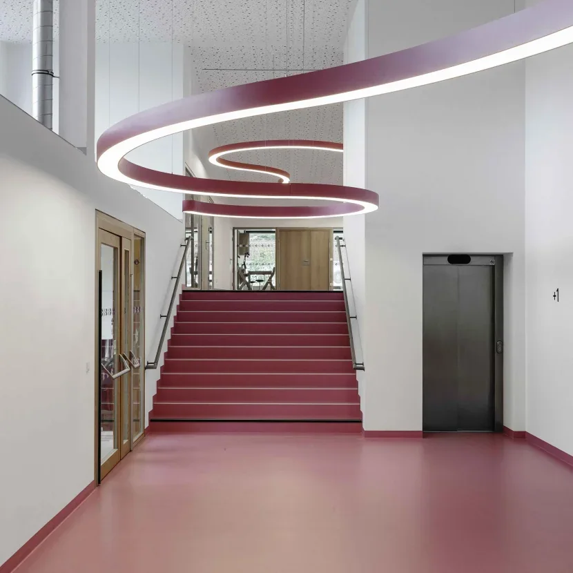 Prolicht: Große helle ringförmige Leuchten in einem Treppenhaus mit rotem Treppenlauf.
