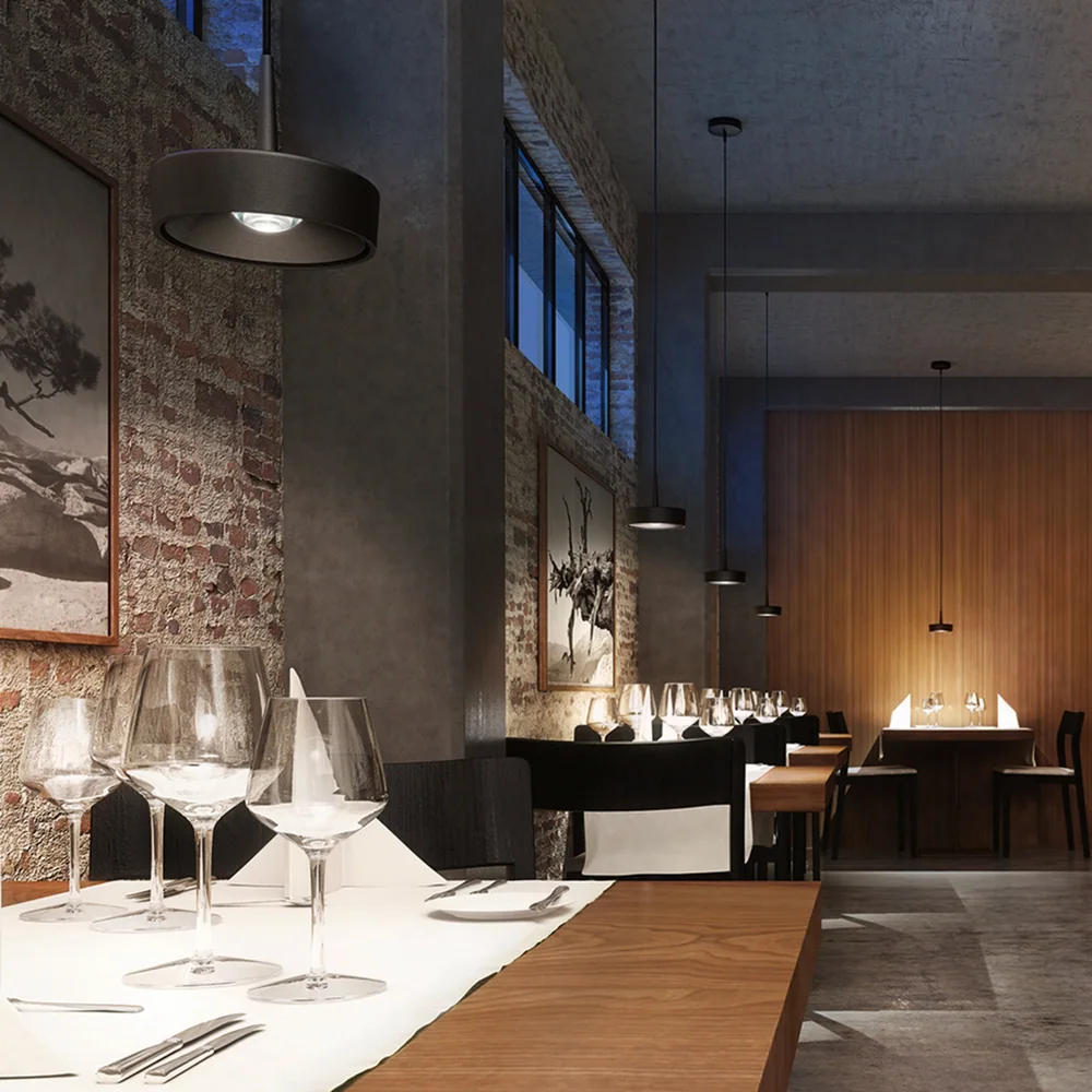 Ribag: Mehrere dunkle breite Pendelleuchten über Tischen und Theke in einem Restaurant mit Steinwand.