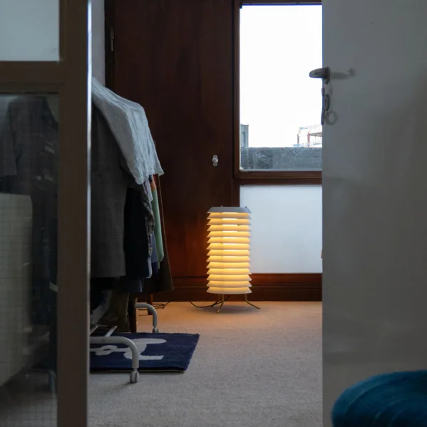 Santa & Cole: Gerippte zylindrische Leuchte neben Möbeln und einem hohen Fenster in einem Wohnraum.