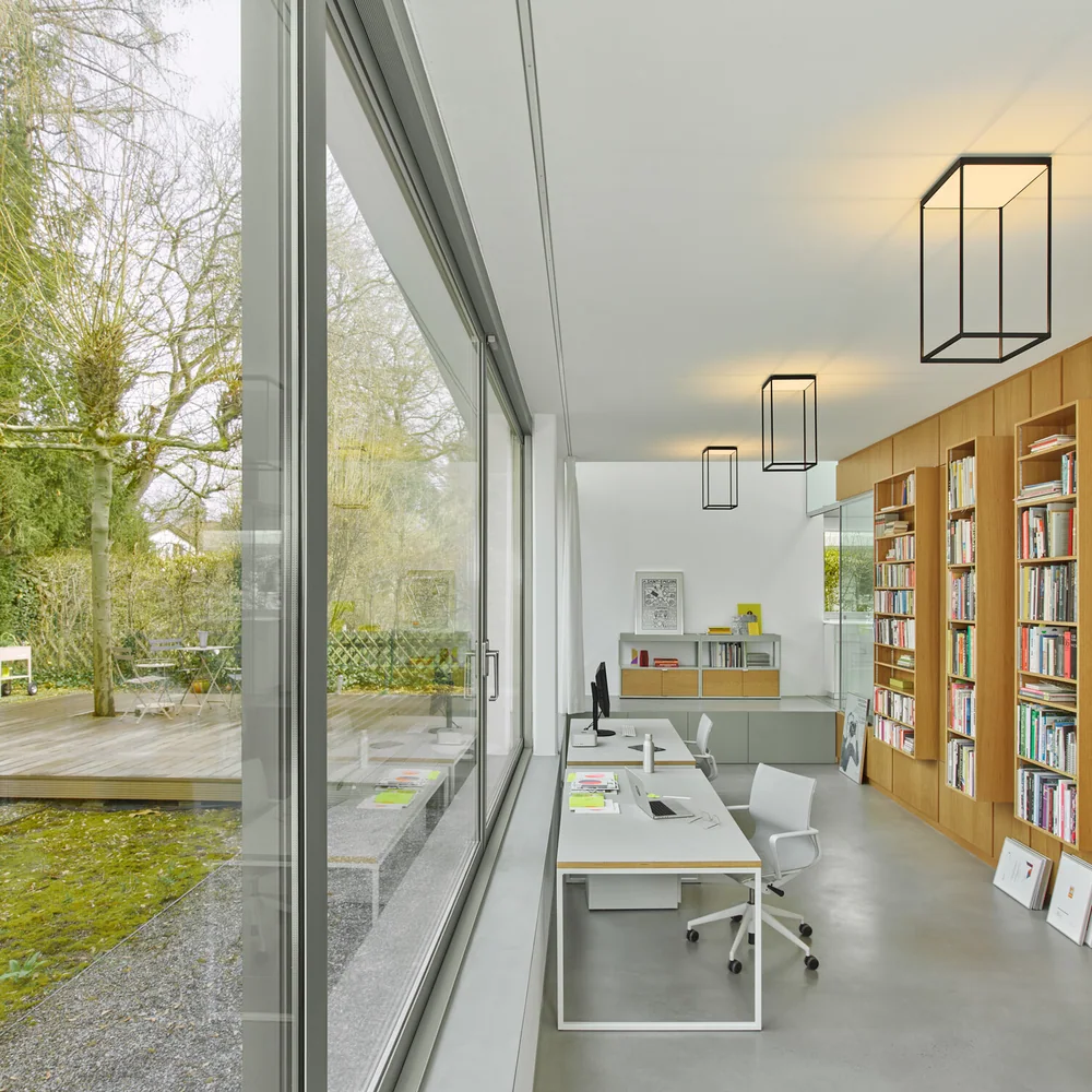 serien.lighting: Mehrere kantige rahmenförmige Deckenleuchten in einem hellen Raum mit langen Fensterflächen und Einbaumöbeln.
