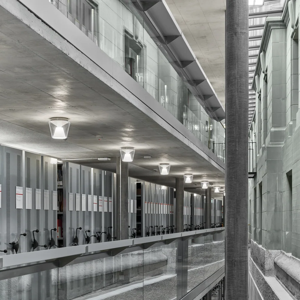 serien.lighting: Viele kompakte helle Deckenleuchten begleiten einen langen Flur mit Glasflächen.