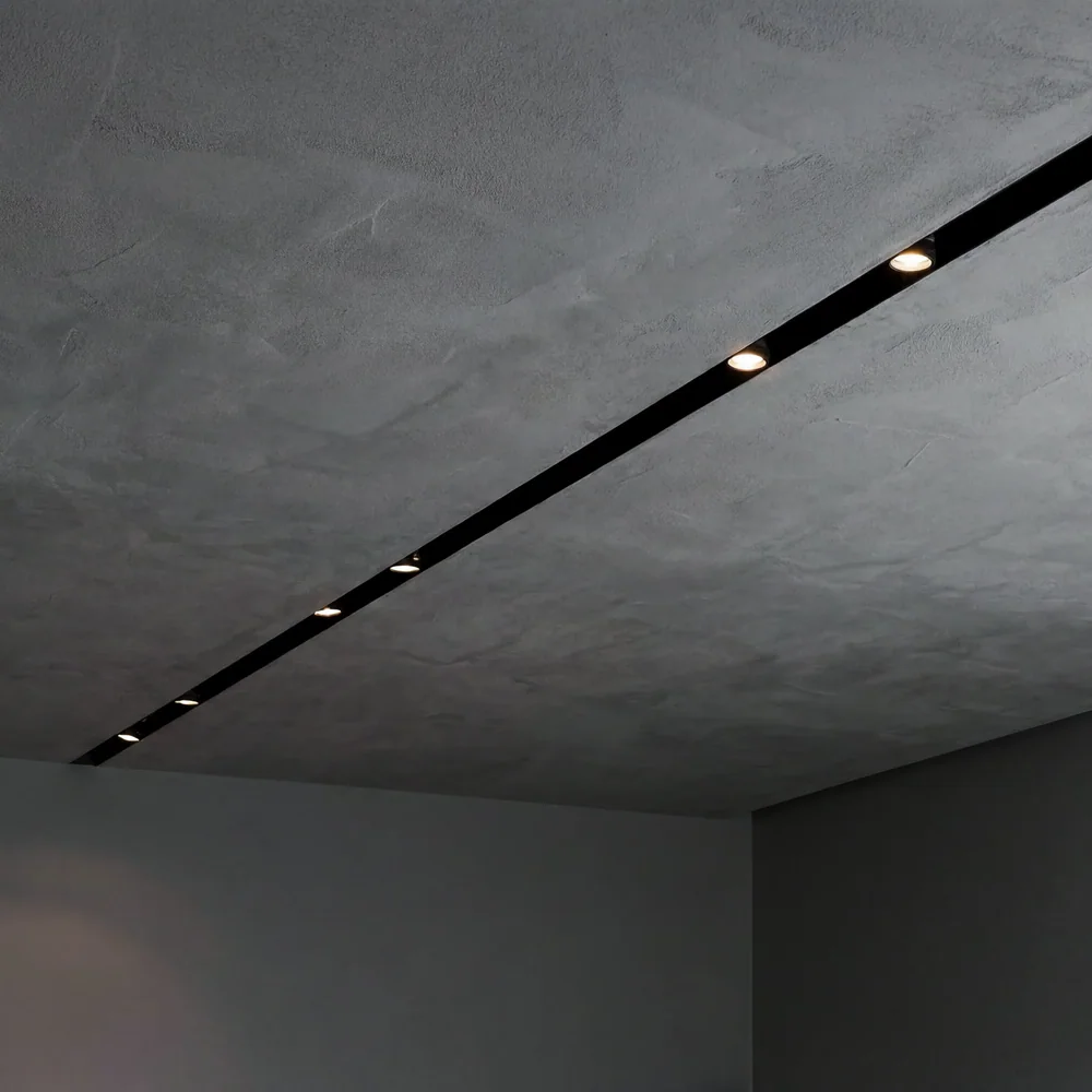 Viabizzuno: Schmaler schwarzer Schlitz mit mehreren kleinen Lichtpunkten in einer grauen Decke.